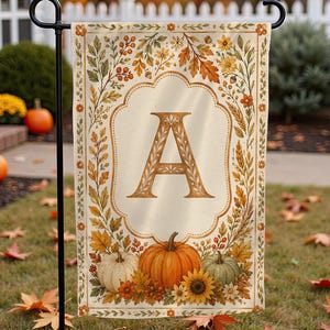 May include: A rectangular garden flag featuring a cream-colored background with a central letter A in a decorative serif font. The border is adorned with autumn leaves, berries, and flowers, with three pumpkins and a sunflower at the bottom.