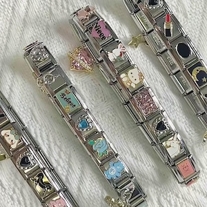 May include: Several stainless steel charm bracelets with various decorative charms. Charms include hearts, flowers, a unicorn, a lipstick, and the word "Believe". Some charms are pink, blue, and white.