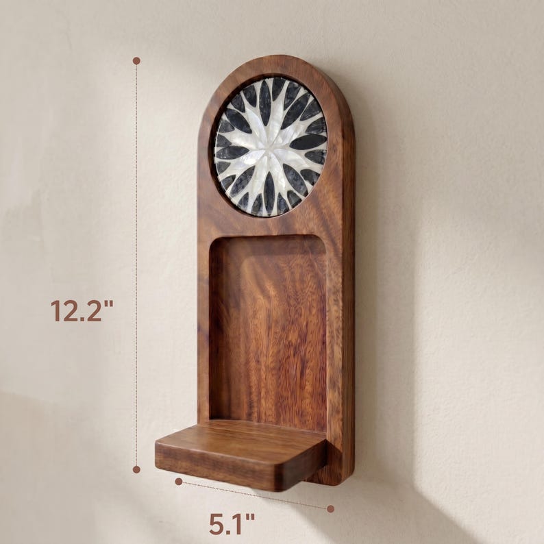 May include: A wooden wall shelf with a decorative floral design. The shelf is 12.2 inches tall and 5.1 inches wide. The top section features a circular design with black and white accents. The shelf is made of dark brown wood.