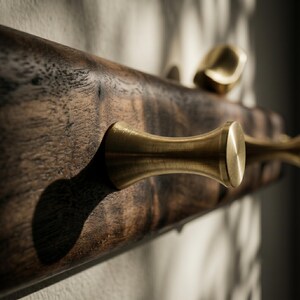 May include: A wall-mounted coat rack featuring a dark brown, natural-grain wooden base with a horizontal orientation. The rack is equipped with multiple protruding, cylindrical brass hooks that have a smooth, brushed metallic finish.