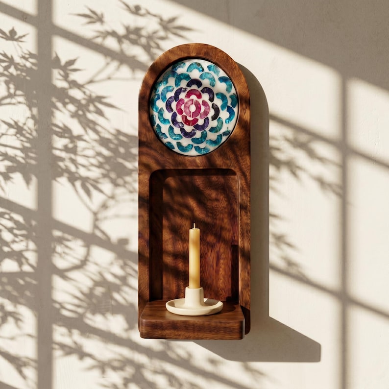 May include: A wooden wall-mounted candle holder with a decorative mosaic tile design in shades of blue, purple, and white. The holder features a small shelf with a lit candle in a cream-colored holder. The wood has a rich, dark brown finish.