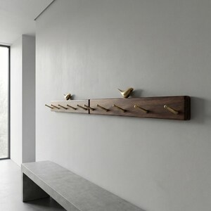 May include: A dark brown wooden coat rack with brass hooks and decorative bird figurines. The rack is mounted on a light gray wall. The hooks are evenly spaced along the bottom edge of the rack.