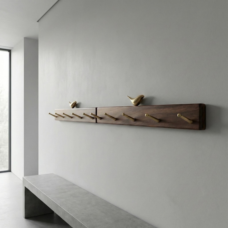 May include: A dark brown wooden coat rack with brass hooks and decorative bird figurines. The rack is mounted on a light gray wall. The hooks are evenly spaced along the bottom edge of the rack.
