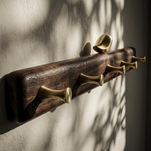 May include: A wall-mounted coat rack featuring a dark brown, natural-edged wooden board with five brass-colored metal hooks. A small, smooth, brass-colored bird-shaped ornament is attached to the top edge of the wooden board.