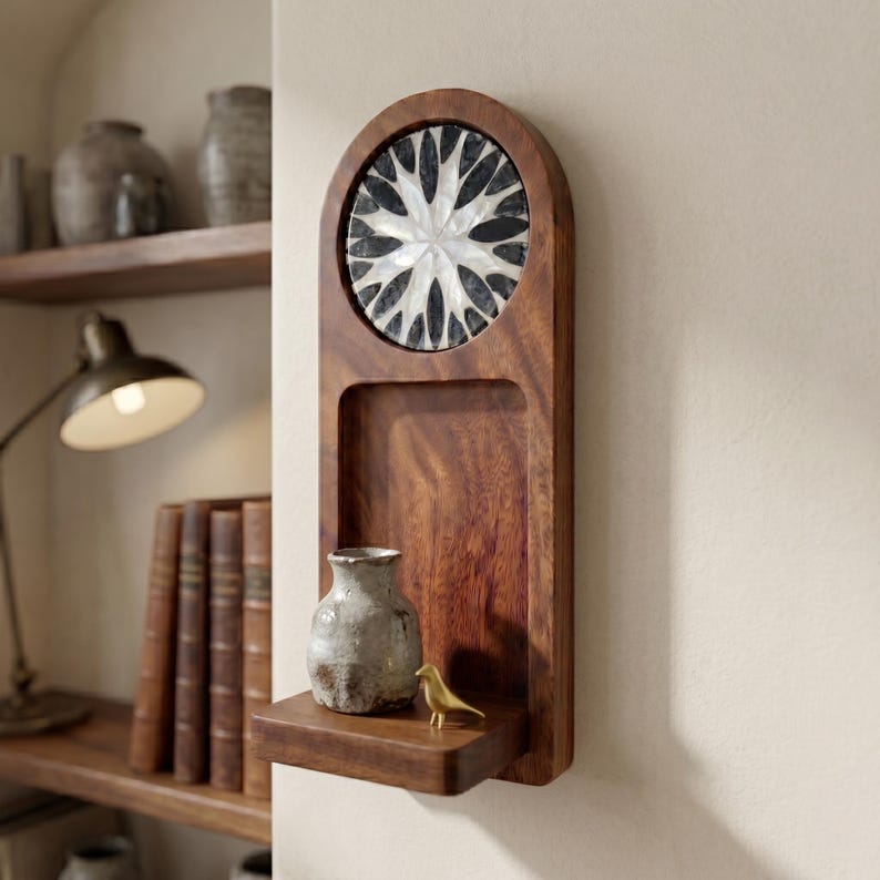May include: A wooden wall shelf with a decorative inlaid design. The shelf features a circular design with black and white accents. A small ceramic vase and a gold bird figurine sit on the shelf.