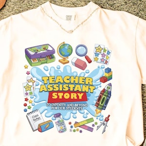 Puede incluir: Una camiseta de color crema con un estampado gráfico con el texto "TEACHER ASSISTANT STORY TO INFINITY AND BEYOND FOR OUR STUDENTS" rodeado de ilustraciones de un globo terráqueo, lupa, cohete, cuaderno y varios útiles escolares.