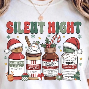 May include: White t-shirt with the text "SILENT NIGHT" in red and green. The shirt features illustrations of medicine bottles with Santa hats, labeled "Gingerbread Versed", "Sugar Cookie Ativan", "Hazelnut Haldol", and "Peppermint Mocha Propofol".