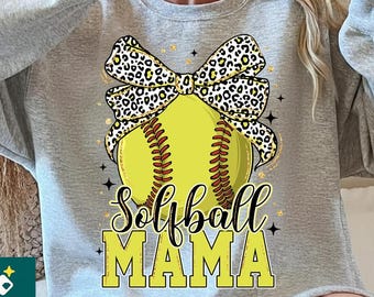 May include: A gray sweatshirt featuring a yellow softball with brown stitching and a leopard print bow. The text "Softball MAMA" is in yellow block letters. The sweatshirt is a casual, sporty style.