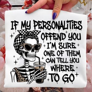 May include: White t-shirt with a graphic of a skeleton wearing sunglasses and a checkered bandana, drinking from a cup. The text reads: "IF MY PERSONALITIES OFFEND YOU + I'M SURE + ONE OF THEM CAN TELL YOU WHERE + TO GO."