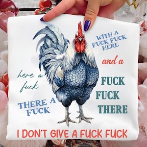 Op de afbeelding: Wit t-shirt met een gedetailleerde illustratie van een haan met blauwe en witte veren en een rode kam. Tekst bevat zinnen als "I don't give a fuck fuck" en "here a fuck".