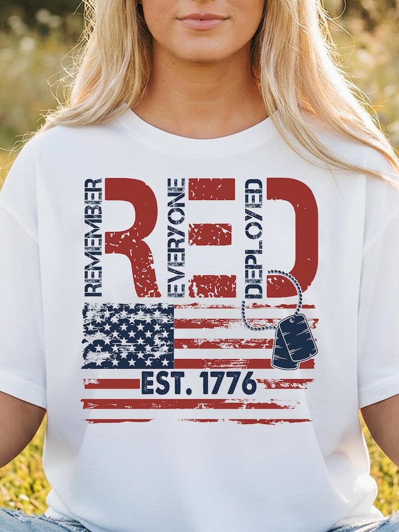 K&ouml;nnte beinhalten: Wei&szlig;es T-Shirt mit patriotischem Design. Das Design zeigt den Text "REMEMBER RED EVERYONE DEPLOYED" in Rot, zusammen mit einer amerikanischen Flagge und Erkennungsmarken. Der Text "EST. 1776" ist ebenfalls enthalten.