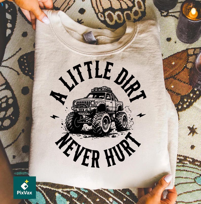 May include: A beige sweatshirt featuring a black graphic of a monster truck with the text "A Little Dirt Never Hurt." The design includes lightning bolts and a detailed illustration of the vehicle.