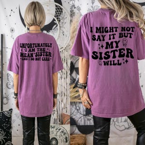 May include: A purple t-shirt with the text "UNFORTUNATELY I AM THE MEAN SISTER AND I DO NOT CARE" on the front and "I MIGHT NOT SAY IT BUT MY SISTER WILL" on the back. The shirt is a casual style.