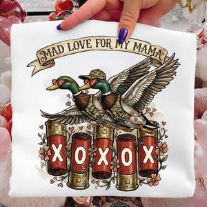 Op de afbeelding: Witte sweatshirt met een afbeelding van twee eenden met zonnebrillen en hoeden, met de tekst "MAD LOVE FOR MY MAMA". De eenden staan op vier hagelpatronen met de letters "XOXO".