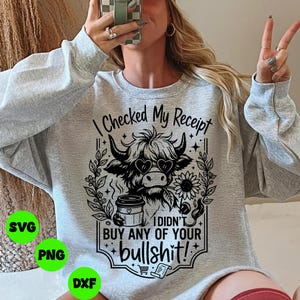 May include: A light gray sweatshirt with a graphic design. The design features a Highland cow wearing heart-shaped sunglasses, a coffee cup, and the text "I Checked My Receipt, I Didn't Buy Any of Your Bullshit!"