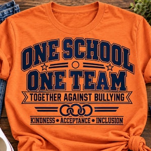 以下が含まれることがあります： ONE SCHOOL ONE TEAM TOGETHER AGAINST BULLYINGという紺色の文字、3つの重なり合う円のグラフィック、そしてKINDNESS、ACCEPTANCE、INCLUSIONという単語がプリントされた、オレンジ色の半袖Tシャツ。