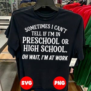 May include: Black t-shirt with white text: "SOMETIMES I CAN'T TELL IF I'M IN PRESCHOOL OR HIGH SCHOOL. OH WAIT, I'M AT WORK." The shirt is hanging on a black hanger with other shirts in the background.