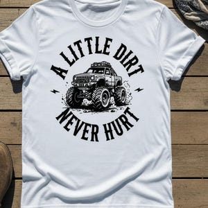 May include: White t-shirt with a black graphic of a monster truck and the text "A Little Dirt Never Hurt". The design features a detailed illustration of the vehicle with large tires and lightning bolts.