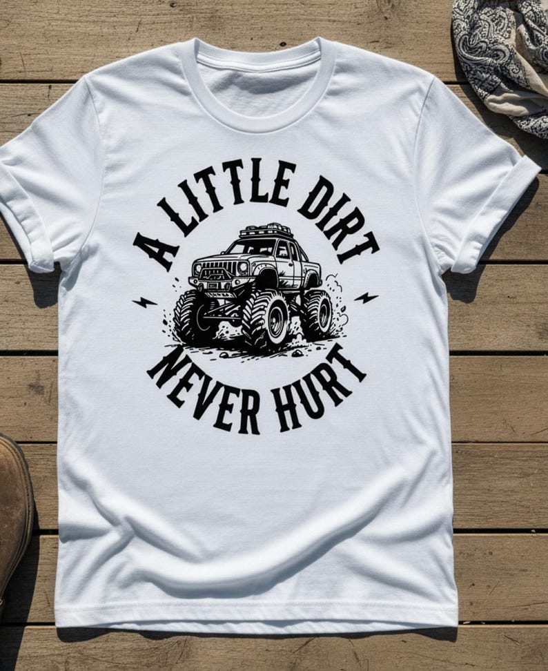 May include: White t-shirt with a black graphic of a monster truck and the text "A Little Dirt Never Hurt". The design features a detailed illustration of the vehicle with large tires and lightning bolts.