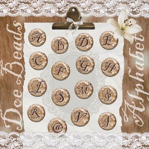 May include: A collection of circular beige beads featuring dark brown script letters A, B, D, E, C, F, G, H, I, S, M, &, R, V, J, and @. The beads are arranged on a white paper sheet held by a metal clip, decorated with a white lily and lace.