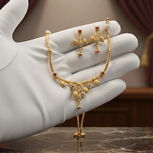 Könnte beinhalten: Ein goldfarbenes Halsketten- und Ohrring-Set. Die Halskette hat ein filigranes Design mit kleinen roten und klaren Edelsteinen. Die Ohrringe spiegeln das Design der Halskette wider, mit einer ähnlichen Anordnung von Edelsteinen.