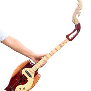 Könnte beinhalten: Ein handgefertigtes Musikinstrument aus Holz mit einem einzigartigen, geschwungenen Design. Das Instrument hat einen rotbraunen Korpus mit einem hellen Holzakzent, ein Griffbrett und eine dekorative, geschnitzte Kopfplatte. Das Instrument wird von einer Person gehalten.