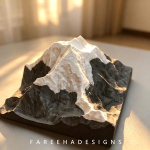 May include: A three-dimensional mountain sculpture featuring a textured black base and a white snow-capped peak. The base of the object displays the text FAREEHADESIGNS in white capital letters. The design depicts a mountain range with ridges.