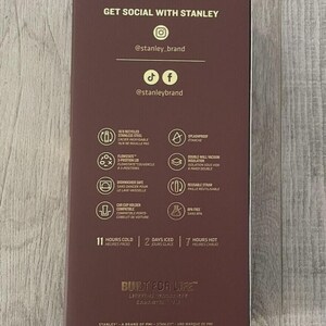 May include: A dark maroon rectangular product box featuring gold text and icons. The text includes GET SOCIAL WITH STANLEY, @stanley_brand, BUILT FOR LIFE, and product specifications such as 18/8 recycled stainless steel, splashproof, and BPA free.