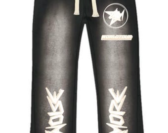 May include: Black denim-style sweatpants with a faded wash effect. Features a white drawstring, a white logo with the text "WORLD TOUR", and white decorative text on the lower legs. The pants have a raw hem.