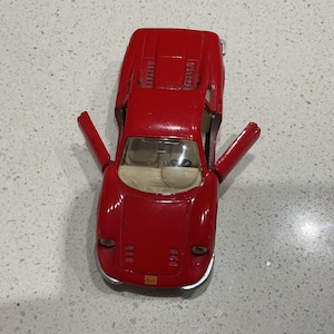 Könnte beinhalten: Ein rotes Spielzeugauto mit geöffneten Türen. Das Auto hat ein schlankes Design mit beigem Innenraum. Die Türen sind geöffnet und zeigen die Innendetails. Es ist ein klassisches Spielzeugfahrzeug.