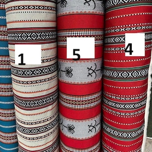 Puede incluir: Primer plano de varios rollos de tela estampada. Las telas presentan diseños geométricos en varios colores, incluyendo rojo, blanco, negro y verde azulado. Algunos rollos tienen patrones de inspiración tribal, otros diseños a rayas.