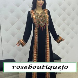 May include: A long black dress with intricate embroidery in red, gold, and cream colors. The embroidery is concentrated around the neckline, down the front, and on the sleeves. The text "roseboutiquejo" is displayed at the bottom.