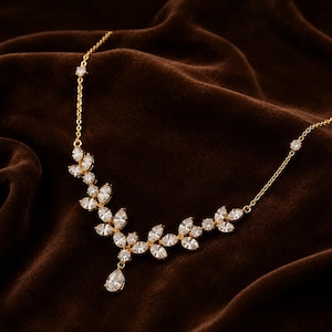 May include: A gold-toned necklace featuring a delicate chain adorned with a central cluster of marquise-cut clear crystals arranged in a leaf-like pattern, finished with a single pear-shaped crystal drop pendant hanging from the centre.