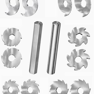 Può includere: Un assortimento di lame per sega e utensili cilindrici in metallo argentato lucido. Le lame hanno varie forme, tra cui circolari con fori centrali esagonali e disegni curvi. Sono visibili anche due utensili cilindrici.