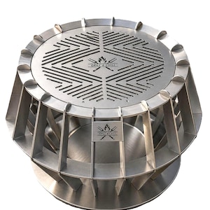 May include: A circular stainless steel grill featuring a geometric slotted cooking surface and a base with vertical support fins. The top and a side plate are engraved with a flame icon and the text GRILL & CHILL. The structure is metallic silver.