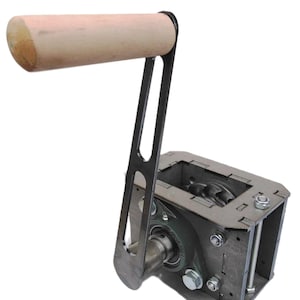 Può includere: Un dispositivo meccanico con un manico cilindrico in legno chiaro attaccato a un braccio metallico e un alloggiamento metallico rettangolare. Il dispositivo ha un complesso meccanismo interno ed è fissato con bulloni e dadi.