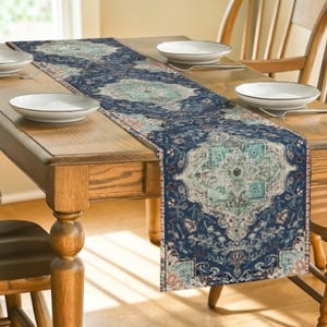 Könnte beinhalten: Marineblauer Tischläufer mit einem detaillierten, verzierten Muster in Türkis-, Beige- und Koralltönen. Der Läufer liegt auf einem Holztisch, mit weißen Tellern und Besteck. Das Design des Läufers hat eine Vintage-Ästhetik.