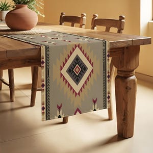 Puede incluir: Camino de mesa gris con un patrón geométrico con formas de diamante en borgoña, negro y beige. El camino de mesa se exhibe sobre una mesa de madera, agregando un toque de estilo suroeste al comedor.
