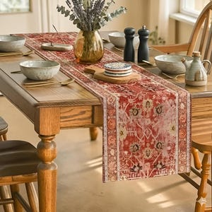 May include: A wooden dining table set with a red patterned table runner. The table is set with bowls, spoons, a vase of flowers, and a small decorative pitcher. The runner has a floral design.