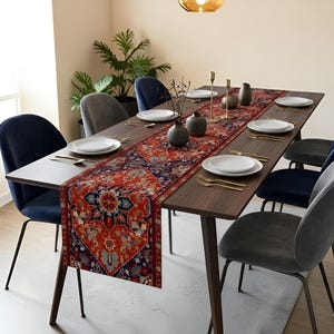 May include: A dark wood dining table set for a meal, featuring a patterned runner in shades of red, blue, and orange. The table is set with white plates, gold cutlery, and decorative vases. Dark blue and gray chairs surround the table.