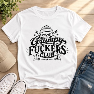 Könnte beinhalten: Ein weißes Kurzarm-T-Shirt mit einem schwarzen Grafikdruck eines Schädels mit Mütze. Der Text lautet Grumpy FUCKERS CLUB, begleitet von Blitz- und Sternsymbolen. Das Design ist mittig auf der Brust des Kleidungsstücks platziert.