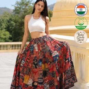 Op de afbeelding: Een wit geribbelde haltertop gecombineerd met een lange, enkellange rok met een levendig, veelkleurig patchworkpatroon in tinten rood, zwart en goud. De rok heeft een hoge taille en een wijd, vloeiend silhouet met ingewikkelde prints.