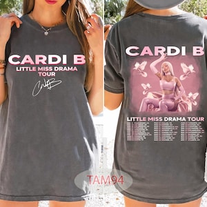May include: Dark gray t-shirt featuring the text "Cardi B Little Miss Drama Tour" in pink and white. The front of the shirt displays the artist's name and tour title. The back of the shirt has a graphic of Cardi B and tour dates.