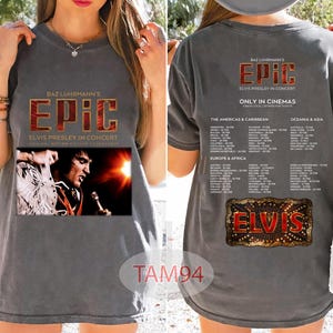 May include: Gray t-shirt featuring the text "BAZ LUHRMANN'S EPIC ELVIS PRESLEY IN CONCERT" with an image of Elvis Presley. The back of the shirt has tour dates and the word "ELVIS" in a decorative frame.