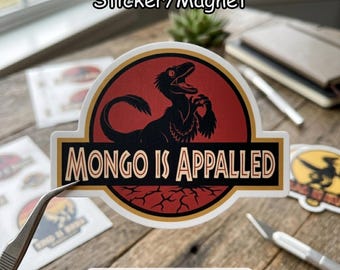 May include: A sticker or magnet featuring a black dinosaur silhouette on a red background, with the text "MONGO IS APPALLED" in a yellow and black banner. The design is reminiscent of a movie logo.