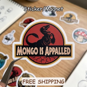 May include: A sticker or magnet with a black dinosaur graphic and the text "MONGO IS APPALLED" in a gold and black design. The sticker is red and white with a black dinosaur graphic. Other stickers are visible in the background.