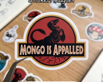 May include: A sticker or magnet with a black dinosaur graphic and the text "MONGO IS APPALLED" in a gold and black design. The sticker is red and white with a black dinosaur graphic. Other stickers are visible in the background.