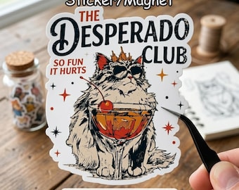 May include: A sticker or magnet featuring a cartoon cat wearing sunglasses and a crown, holding a cocktail with a cherry. The text reads "THE DESPERADO CLUB" and "SO FUN IT HURTS".