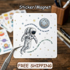 May include: Square sticker or magnet featuring an astronaut illustration. The astronaut is in a spacesuit, floating in space with a moon and stars. Text reads, "I'm an astronaut, you're the moon. I sing to you, I circle you. I stare at you."