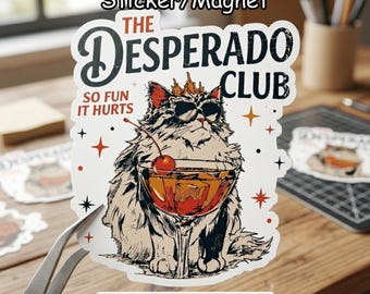 May include: A sticker or magnet featuring a cartoon cat wearing sunglasses and a crown, holding a cocktail with a cherry. The text reads "THE DESPERADO CLUB" and "SO FUN IT HURTS". The design has a vintage, illustrated style.